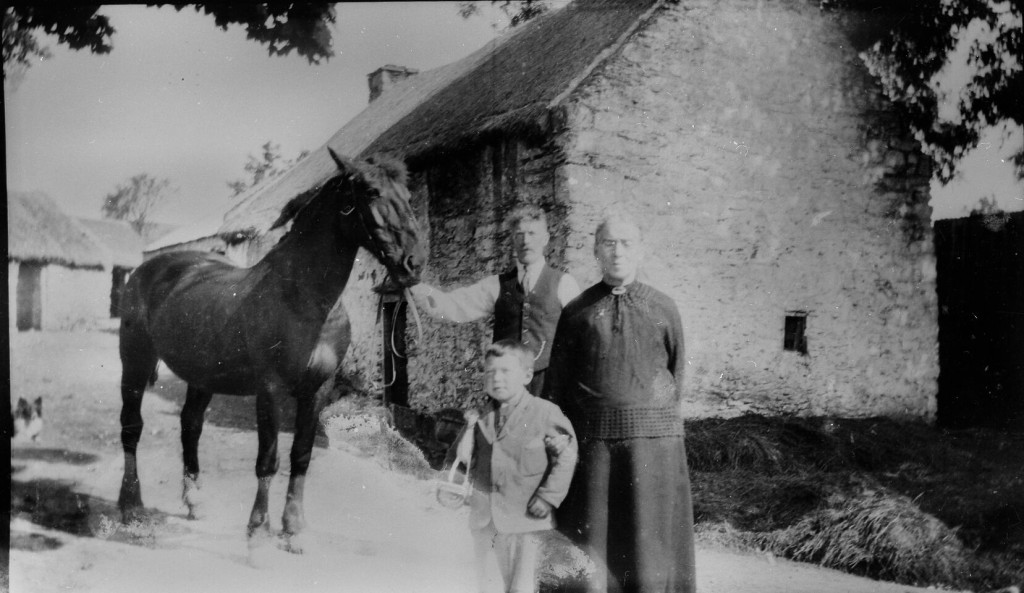A black and white photograph of a family standing in front of a cottage. 