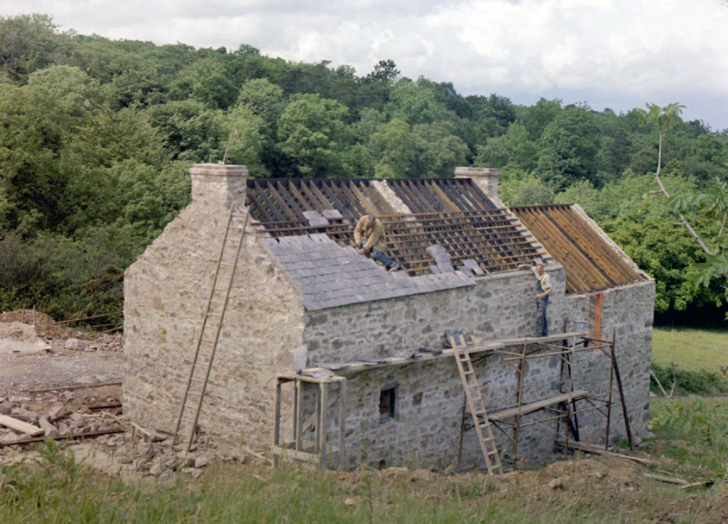 A photograph of a house being rebuilt. Its roof is being retiled.