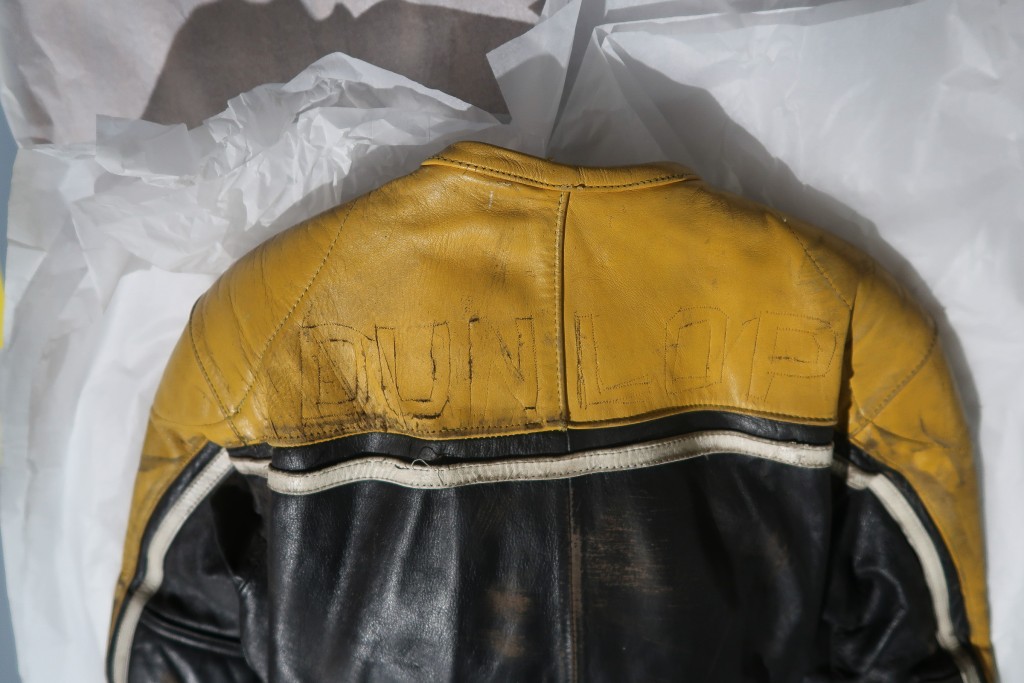 The back of a yellow and black jumpsuit. There are holes where letters were once stitched on, spelling 'Dunlop'.