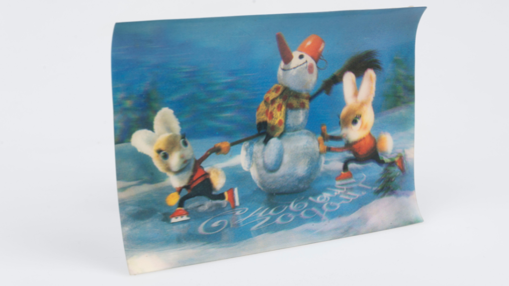 A postcard of cartoon bunnies celebrating the new year. The bunnies are pushing a snowman across a frozen pond. The words 'happy new year' are written in Russian on the ice.