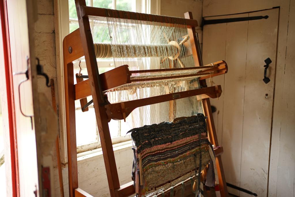 A loom stands in front of a window, with a half-woven blanket still in progress.