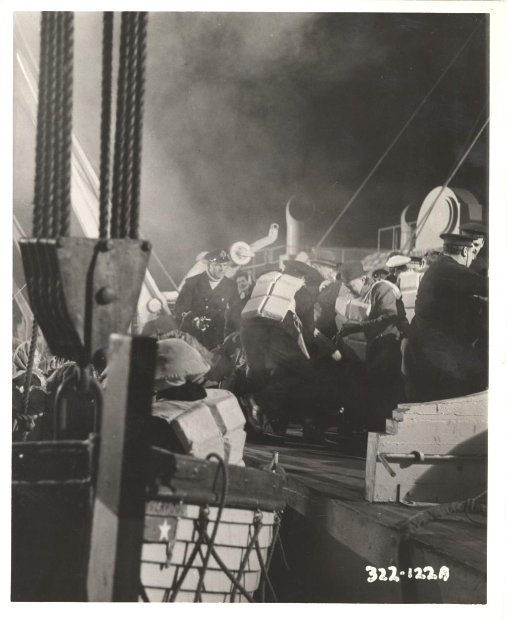 A black and white photograph of a film set. There are actors on the deck of a ship intended to be the Titanic.
