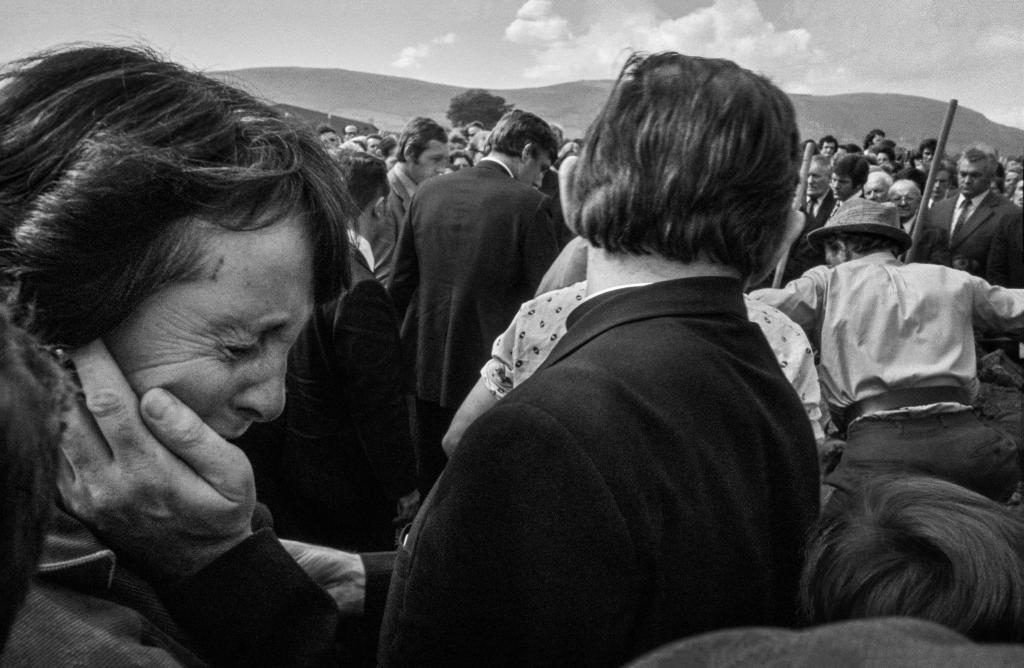 A black and white photograph of a crowd at a funeral. In the foreground we can see a woman deep in mourning. 