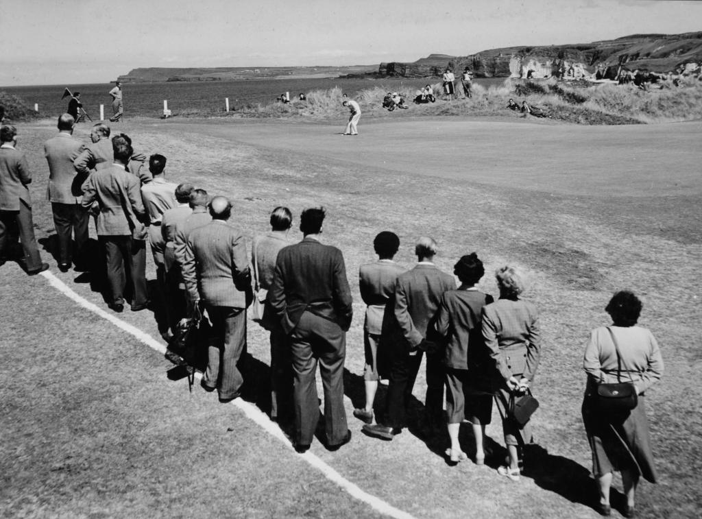A group of spectators watch a man golf at the Royal Portrush Golf Club.