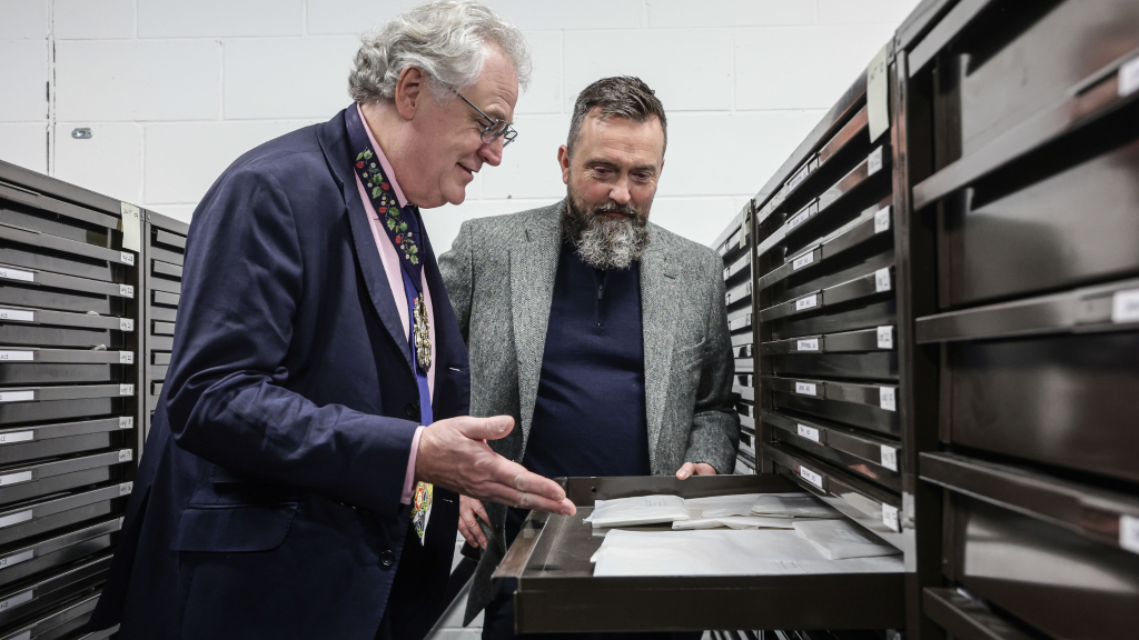 Two people leaning over an opened drawer, looking down into the contents of the drawer and smiling and talking about what they're looking at. The cabinets are black.
