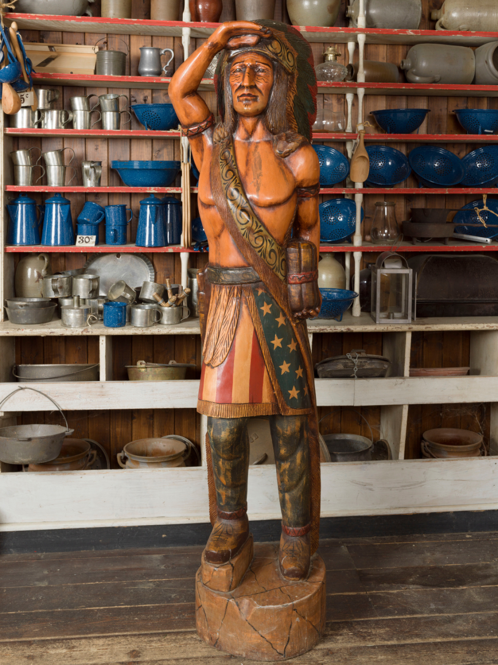 A figure depicting a stereotypical Cigar Store 'Indian', placed in a recreation of a colonial American general store.