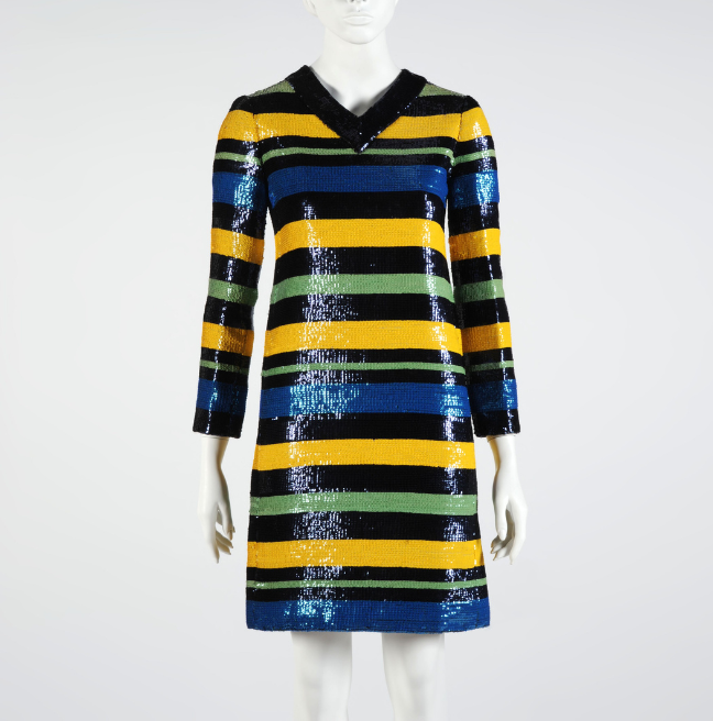 A sequined mini dress on a mannequin. The dress has a shallow v-shaped black collar and sleeves to the wrists. It is patterned with yellow, black, blue and green stripes of alternating widths.