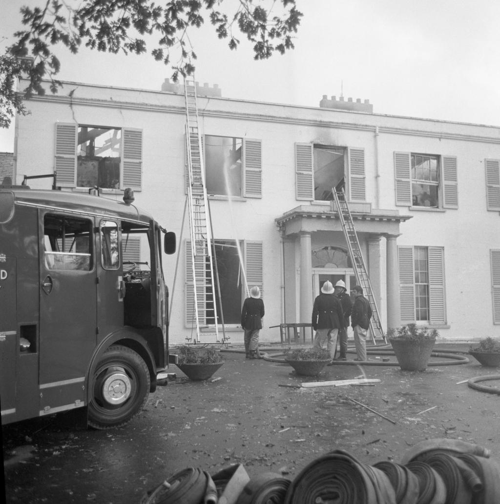 A recently burned building with firefighters at the front, with ladders and a fire engine still present.